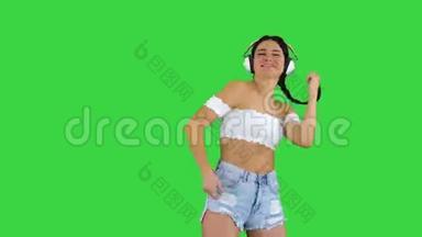 高加索女<strong>模特</strong>戴着<strong>耳机</strong>跳跃，在绿色屏幕上表达快乐的情绪，Chroma键